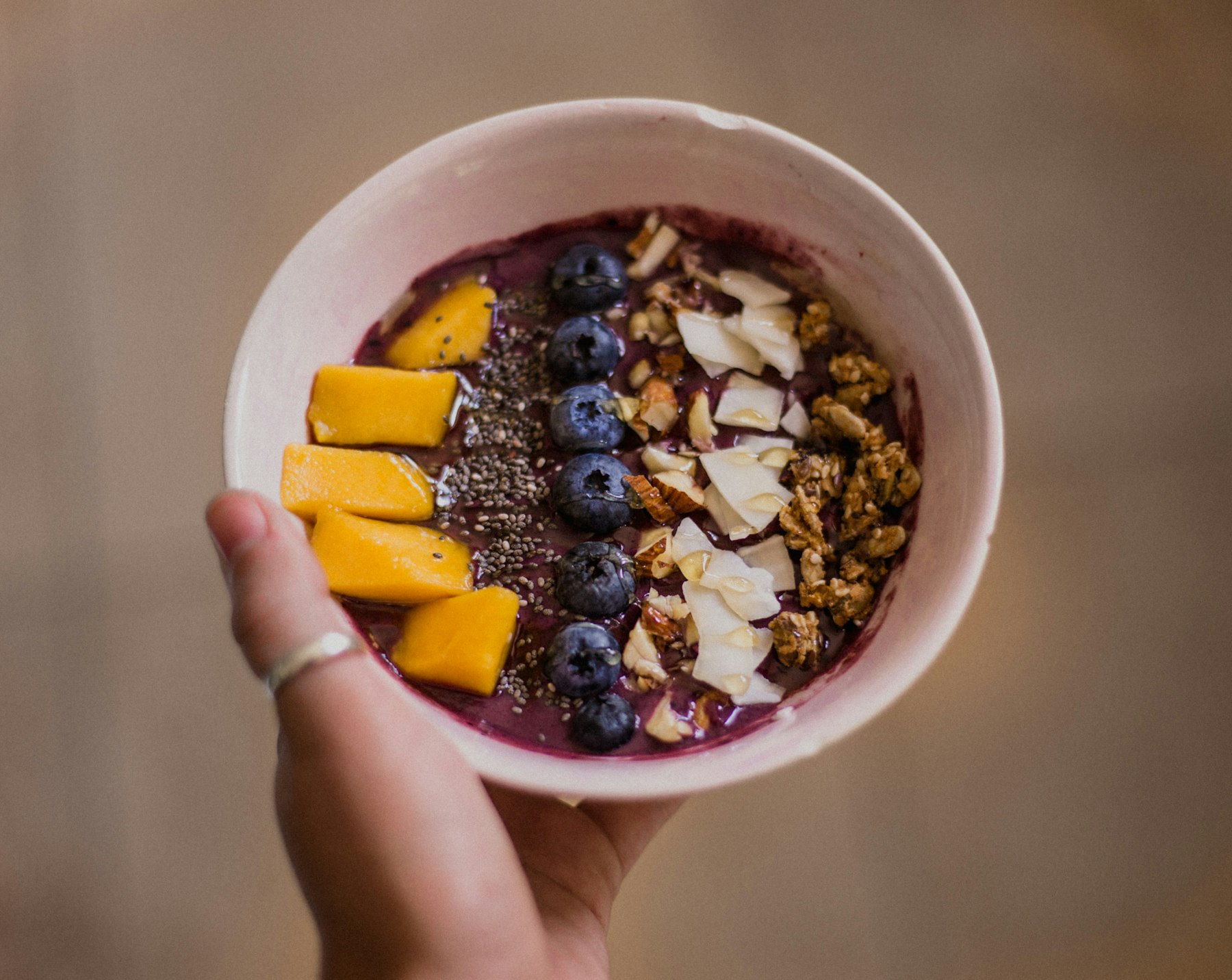 A hand holding a fruit and granola bowl