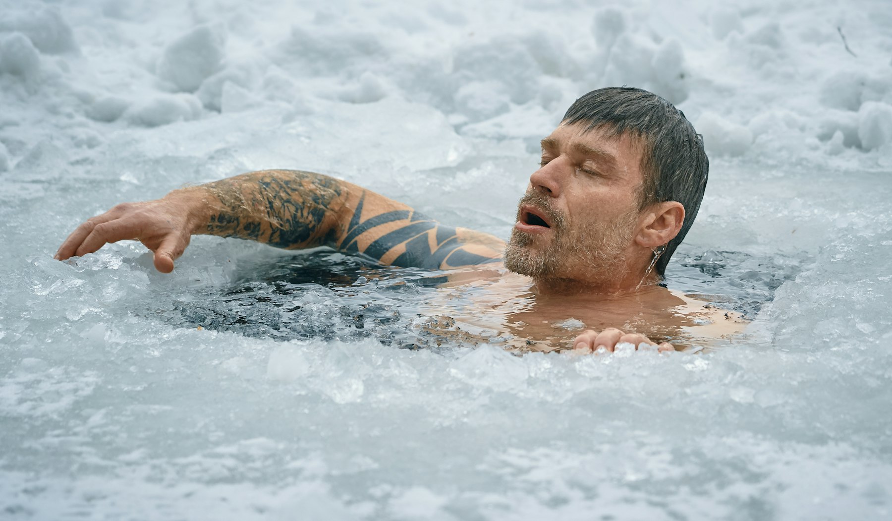 A man in a cold plunge surrounded by snow
